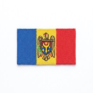 Puede incluir: Parche bordado con la bandera de Moldavia. El parche rectangular tiene franjas verticales azules, amarillas y rojas. La franja amarilla muestra el escudo de armas moldavo, un águila dorada sosteniendo un escudo.