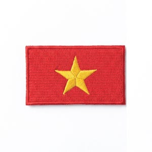 Op de afbeelding: Een rechthoekige rode patch met een gele ster in het midden. De ster heeft vijf punten en is geborduurd. De patch heeft een rode rand en staat tegen een witte achtergrond.