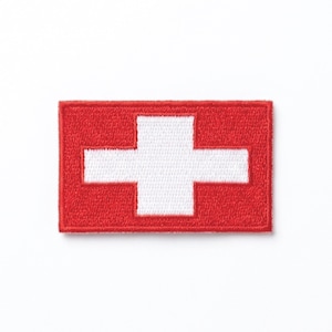 May include: A rectangular red patch with a white cross in the center, representing the Swiss flag. The cross is centered and has equal arms. The patch is likely an embroidered emblem.