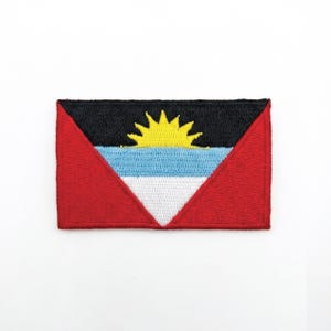 May include: Embroidered patch featuring the flag of Antigua and Barbuda. The design includes a yellow sun, blue and white stripes, and red triangles. The patch is rectangular and has a black top.