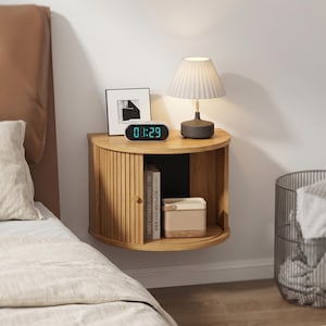 May include: A semi-circular wall-mounted wooden nightstand featuring a sliding tambour door, an open storage compartment, and a flat top surface. The unit holds a pleated table lamp, a digital clock displaying 08:29, and a framed picture.
