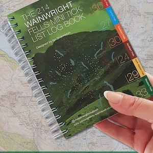 Könnte beinhalten: Ein spiralgebundenes Logbuch mit dem Titel The 214 Wainwright Fells Mini Tick List Log Book, entworfen von Ian Shackleton. Der grüne Einband zeigt eine grafische Karte mit farbigen Reitern für sieben Regionen, nummerierte Listen und eine Website.
