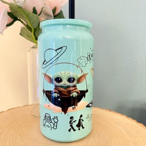 May include: A light teal tumbler with a black straw and lid. The tumbler features a cartoon image of a character from a popular science fiction franchise, along with other space-themed illustrations in black.