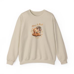 May include: A beige sweatshirt featuring a graphic of two cartoon monkeys hugging. The text "Hang In There" is above the monkeys, with additional text and hearts. The sweatshirt has long sleeves and a crew neck.