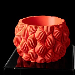 May include: A vibrant orange decorative bowl with a textured, woven-like pattern. The bowl has a round shape with a wide opening and is displayed against a black background. The intricate design adds a unique touch to home decor.