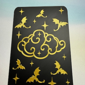 May include: Black rectangular card with rounded corners, featuring a gold cloud, bats, and star design. The bats are in flight, and the stars are four-pointed. The cloud is in the center of the card.