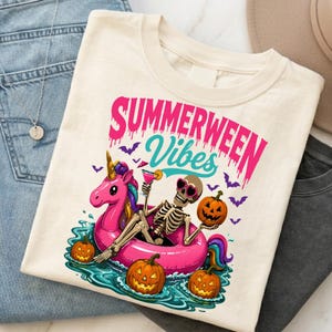 May include: A cream-coloured t-shirt featuring a graphic of a skeleton wearing heart-shaped sunglasses, sitting in a pink unicorn pool float. The design includes three jack-o'-lanterns, purple bats, and the text "SUMMERWEEN Vibes" in pink and teal.