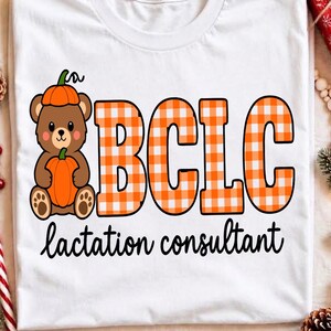 May include: A white t-shirt featuring a brown bear wearing a pumpkin hat and holding a pumpkin. Next to the bear is the text BCLC in an orange and white gingham pattern. Below the bear and text, the words lactation consultant are printed in black.