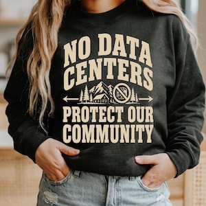 Puede incluir: Sudadera gris oscuro con el texto crema "NO DATA CENTERS PROTECT OUR COMMUNITY". El diseño incluye una escena de montaña, árboles y un edificio con un símbolo de prohibición. Una sudadera de estilo casual.