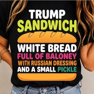 May include: A black t-shirt featuring a graphic of a sandwich with orange bread buns. The text reads: TRUMP SANDWICH, WHITE BREAD, FULL OF BALONEY, WITH RUSSIAN DRESSING, AND A SMALL PICKLE. The lettering uses white, lime green, pink, orange, and teal.