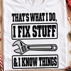 May include: A white t-shirt featuring black text that reads, "THAT'S WHAT I DO, I FIX STUFF & I KNOW THINGS." Between the two phrases is a graphic illustration of a grey and black adjustable wrench centred on the front of the garment.