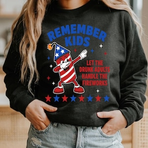 May include: A black long-sleeve sweatshirt featuring a graphic of a firework character dabbing. The text reads REMEMBER KIDS LET THE DRUNK ADULTS HANDLE THE FIREWORKS. The design includes red and blue stars and a firework with a star-spangled pattern.