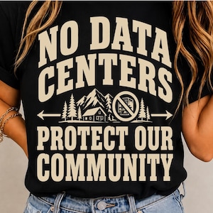 以下が含まれることがあります： 黒いTシャツにベージュの文字で「NO DATA CENTERS PROTECT OUR COMMUNITY」とプリントされています。デザインには家、山、松の木、データセンターのアイコンに重ねられた円形の禁止マーク、そして左右に伸びる2本の矢印が描かれています。