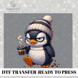 May include: A cartoon penguin with a grumpy expression wearing a striped beanie and holding a coffee cup. The penguin is black, white, and orange, with coffee beans scattered around. The text "DTF TRANSFER-READY TO PRESS" is at the bottom.