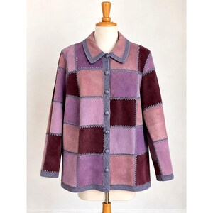 May include: A long-sleeve button-down jacket featuring a patchwork design of square suede panels in various shades of purple, ranging from light lavender to deep plum. The panels are joined by visible grey stitching and a matching grey trim.