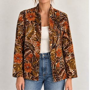 May include: A long-sleeved blazer featuring a vibrant botanical print with orange flowers and brown tropical leaves on a dark background. The jacket has a mandarin collar, an open front design, and is worn over a white top and blue denim jeans.