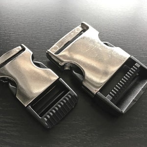 May include: Two silver metal and black plastic side release buckles. The buckles are designed to be used with webbing or straps.
