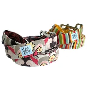 May include: Two dog leashes with different patterns. One leash is brown, gray, pink, and white with a floral pattern. The other leash is multi-colored stripes. Both leashes have a silver clasp and a label that says "The Eclectic Hound".