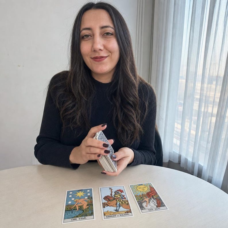 May include: A deck of tarot cards held in hands, with three cards laid out on a table: The Star, Knight of Wands, and The Sun. The cards feature colourful illustrations and text labels at the bottom of each card, depicting a figure, a knight, and a sun.