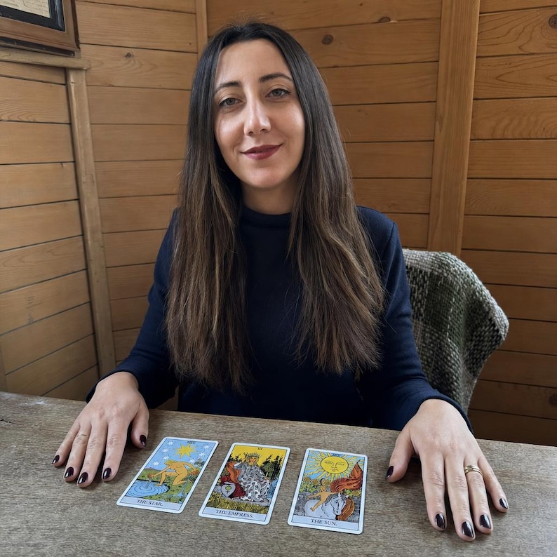 May include: Three tarot cards laid out on a wooden surface. The cards are titled The Star, The Empress, and The Sun. Each card features colourful illustrations with detailed imagery, including a figure by water, a seated queen, and a child on a horse.