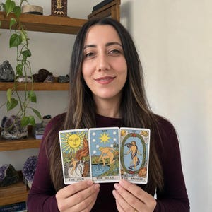 May include: Three tarot cards held in a row, featuring The Sun, The Star, and The World. Each card displays detailed, colourful illustrations with classic imagery, including a sun, a star, and a central figure, all labelled with their respective titles.