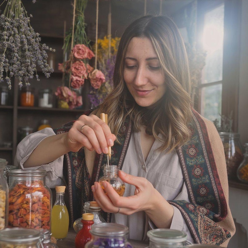 May include: A person is shown in a shop, holding a small glass bottle with a wooden stopper. The bottle contains a golden liquid. Various jars and bottles with colorful contents are visible, along with dried flowers, suggesting a natural apothecary or herbalist theme.