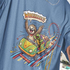 May include: A light blue t-shirt featuring a cartoon sloth, turtle, and snail riding a roller coaster. The sloth is raising its arms with the text "WHEEEEE!!" above. The roller coaster car is green and yellow.