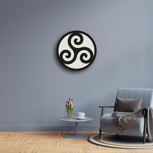 May include: A circular wall art piece featuring a black triskelion symbol centered on a cream-colored background. The design consists of three interlocking spiral arms radiating from the center, enclosed within a solid black circular border frame.
