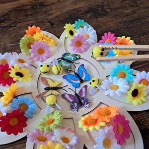Peut inclure: Un artisanat en forme de fleur en bois avec des fleurs artificielles colorées, des papillons et des décorations d'abeilles. Les fleurs sont dans les tons de jaune, orange, rose, bleu et blanc. Les papillons ont divers motifs et couleurs.