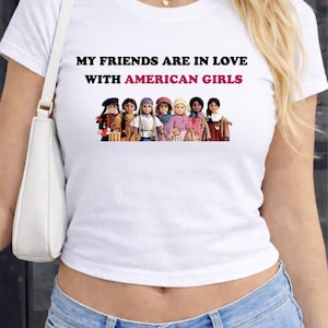 May include: White t-shirt with the text "MY FRIENDS ARE IN LOVE WITH AMERICAN GIRLS" in black and pink. Below the text is a graphic of several dolls. The person is wearing blue jeans and a white purse.