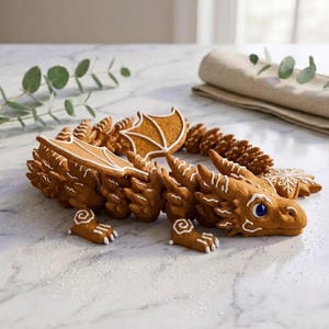 May include: A gingerbread dragon cookie featuring intricate white icing details, textured scales, and a single blue eye. The dragon is shaped with wings, a long tail, and clawed feet, decorated with white icing swirls and lines on a light brown surface.