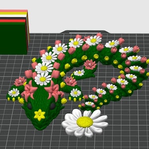 May include: A green, floral-decorated snake-shaped sculpture with white daisies, pink tulips, and yellow accents. A stack of colorful blocks sits to the left. A large white daisy with a yellow center is at the bottom.