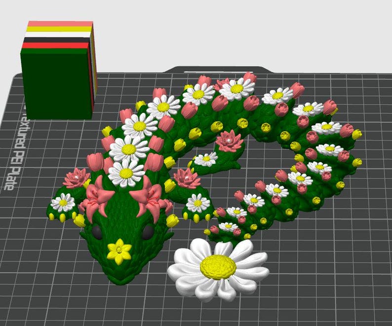 May include: A green, floral-decorated snake-shaped sculpture with white daisies, pink tulips, and yellow accents. A stack of colorful blocks sits to the left. A large white daisy with a yellow center is at the bottom.