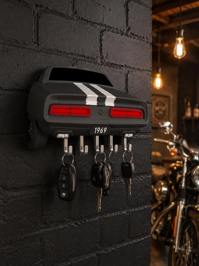 May include: A wall-mounted key holder shaped like the rear of a black 1969 muscle car. It features two white racing stripes, red taillights, and a license plate reading 1969. Five silver metal hooks extend from the bottom, holding various keys.