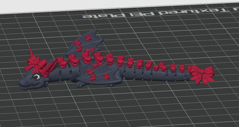 May include: A dark gray articulated dragon figurine featuring a series of bright red bows attached along its back, wings, and tail, with a large red bow positioned on its head and another at the tip of its tail, all set against a grid background.