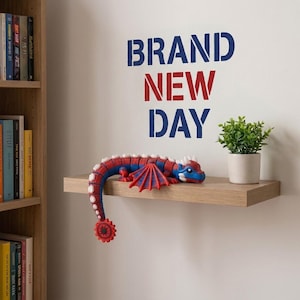 May include: A blue and red articulated dragon toy with white spikes sits on a wooden shelf next to a small potted green plant. Above the shelf, the wall features the text BRAND NEW DAY in blue and red stencil-style lettering.