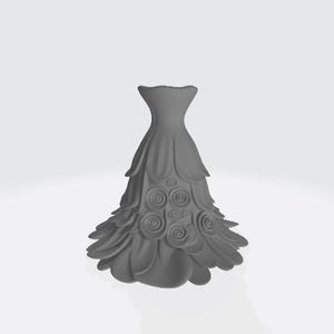 Puede incluir: Un jarr&oacute;n decorativo gris, estilizado en forma de vestido. Presenta detalles en capas con forma de p&eacute;talos y adornos con forma de rosas. El dise&ntilde;o es sim&eacute;trico y se encuentra sobre un fondo blanco liso.