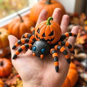 May include: A spider figurine featuring a black body with two large blue eyes and orange fangs, with eight articulated legs striped in black and orange. A carved orange jack-o'-lantern pumpkin sits securely on the back of the spider.