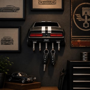 May include: A wall-mounted key holder shaped like the rear of a black 1969 muscle car with white racing stripes, red taillights, and a license plate reading 1969. The unit features four silver metal hooks for hanging keys, with two key fobs attached.
