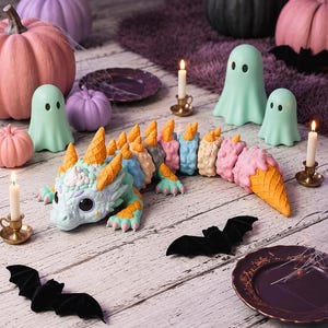 May include: A multi-colored articulated dragon figurine featuring a textured body with pastel blue, pink, and beige segments, topped with orange waffle cone-shaped spikes and a matching cone tail tip, with large black eyes and small pink claws.