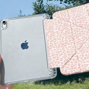 May include: A clear iPad case with a pink leopard print cover. The iPad has a silver back with the Apple logo. The case is held in front of a green background. The text "CuteXCaseDesign" is visible.