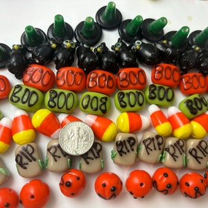 Könnte beinhalten: Eine Sammlung von Halloween-Glasperlen, darunter schwarze Katzen, Hexenhüte, Maisbonbons und Perlen mit den Worten "BOO" und "RIP" darauf.