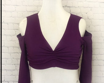 May include: A purple cold shoulder crop top with long sleeves. The top has a deep V-neck and a gathered detail at the front.