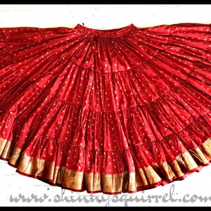 May include: A red, multi-layered skirt with gold trim. The skirt is made of a soft, flowing fabric and has a gathered waist.