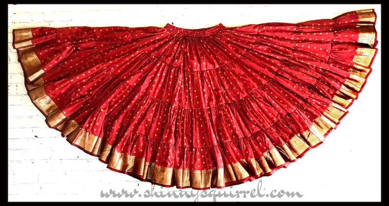 May include: A red, multi-layered skirt with gold trim. The skirt is made of a soft, flowing fabric and has a gathered waist.