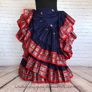 May include: A navy blue dance skirt with multiple layers of red and gold trim. The skirt has a gathered look and is designed for belly dancing or other performance styles.
