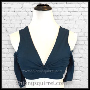 Peut inclure: Un haut court bleu sarcelle à épaules dénudées avec un décolleté en V profond et un détail torsadé à l'avant. Le haut porte une adresse de site Web imprimée sur le devant : www.shinnyssquirrel.com