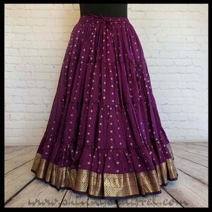 May include: A long, purple skirt with gold accents and a gold trim. The skirt has multiple layers and a gathered waistband.