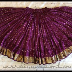 May include: A purple and gold skirt with a layered design and gold trim. The skirt is made of a soft, flowing fabric and has a gathered waist.