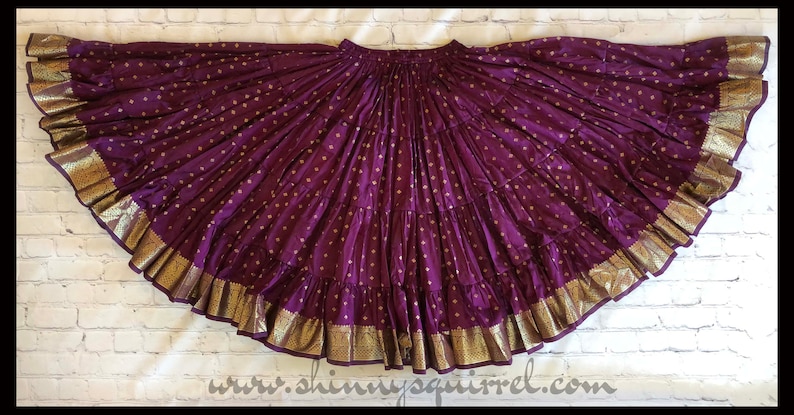 May include: A purple and gold skirt with a layered design and gold trim. The skirt is made of a soft, flowing fabric and has a gathered waist.